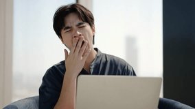 Young Asian man sitting at desk with laptop yawning, showing signs of boredom at a modern office, Tired male having dull distant job, feeling lazy, sleepy guy feel fatigue taking nap near computer - Powered by Shutterstock - Get 15% off with code: PIKWIZARD15