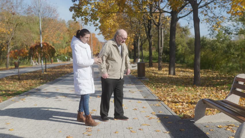 An elderly man experiences a heart attack in the park, and his compassionate caregiver helps him sit on a bench, emphasizing the importance of elderly support.