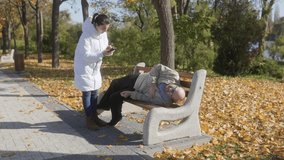 An elderly man clutching his chest in pain is seated on a park bench. A concerned woman passing by calls for medical assistance, recognizing his urgent need. - Powered by Shutterstock - Get 15% off with code: PIKWIZARD15