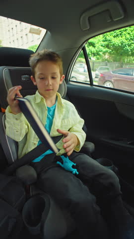 Young Boy Studying and Reading in a Child Car Seat with Parents Driving Learning on the Road to School or During Family Travel. High quality 4k footage