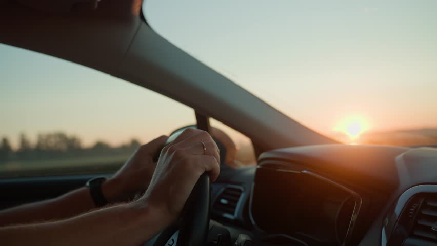 Male driver driving car, inside view. Man driving car on highway road at sunrise. Close-up of driver hands turning steering wheel
