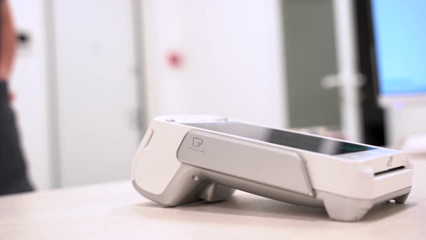 Pay by phone on electronic payment machine or card reader. E-money at cashless wallet. Female hand with pos-terminal and credit card closeup. Client pays for the procedure in modern beauty clinic.