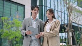 Two asian coworkers standing outside in front of office buildings discuss about business plan and looking at tablet.handsome asia man and beautiful asian woman as business partners working at outdoor - Powered by Shutterstock - Get 15% off with code: PIKWIZARD15