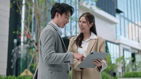 Two asian coworkers standing outside in front of office buildings discuss about business plan and looking at tablet.handsome asia man and beautiful asian woman as business partners working at outdoor - Powered by Shutterstock - Get 15% off with code: PIKWIZARD15