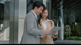 Two asian coworkers standing outside in front of office buildings discuss about business plan and looking at tablet.handsome asia man and beautiful asian woman as business partners working at outdoor - Powered by Shutterstock - Get 15% off with code: PIKWIZARD15