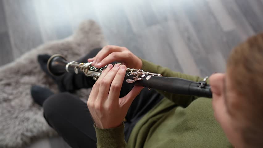 Clarinet player closeup top view. Clarinetist hands playing flute woodwind music instrument at home, selective focus. Musical instruments. Guy plays the oboe in education classroom. Hobby. 