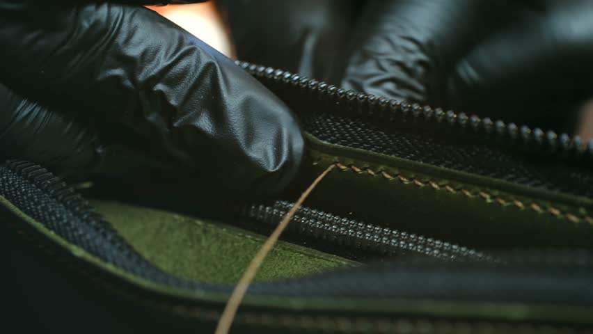 Tailor in latex gloves stitches leather wallet cover in old fashioned workshop closeup. Master connects classic purse for money with threads