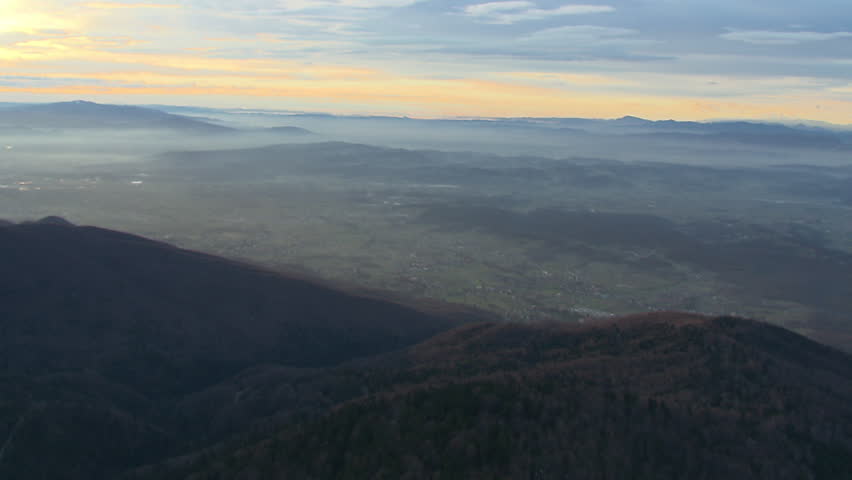 Slopes of a mountain and green valley at sunrise. Aerial helicopter shot.