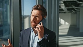 Bearded ceo speaking cellphone modern architecture building closeup. Brunette businessman calling partners discussing business portrait. Elegant man boss talking smartphone at panoramic windows office - Powered by Shutterstock - Get 15% off with code: PIKWIZARD15