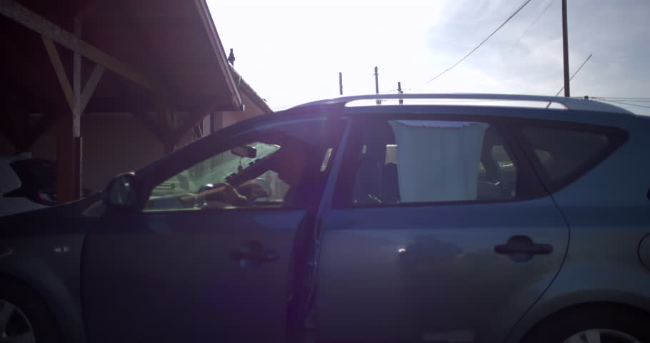 Man exiting car from driver's seat in residential driveway, completing a task or returning home, with focus on casual activity and end of journey