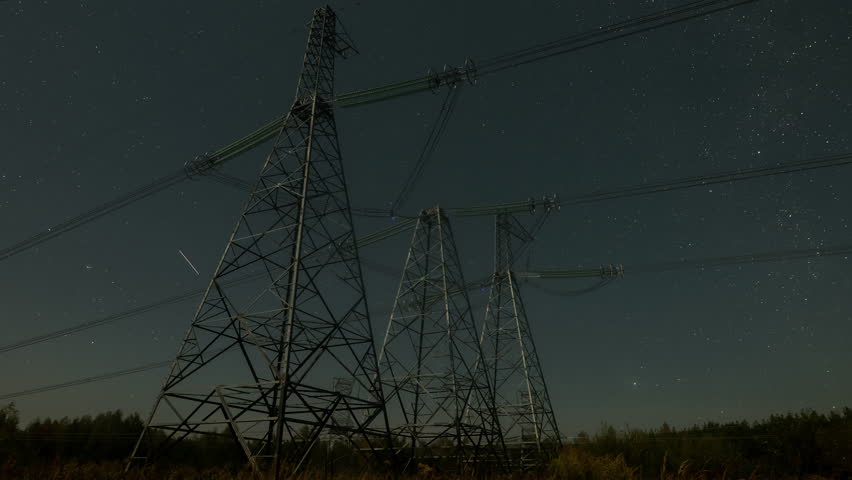 Nighttime view of high voltage power lines against the backdrop of moving stars in the night sky on a moonlit night. Concept of electricity and energy generation. Time lapse