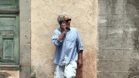 Elderly man walking in a city street answering the mobile phone. Attractive senior man walking in Spanish village, close-up of smiling casual dressed man on urban background - Powered by Shutterstock - Get 15% off with code: PIKWIZARD15