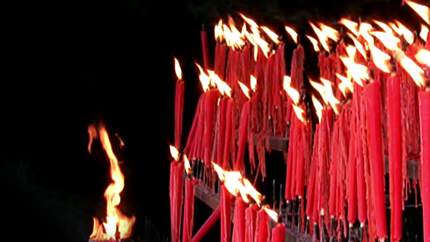 A lot of red ritual candles are burning on a black background. The flames