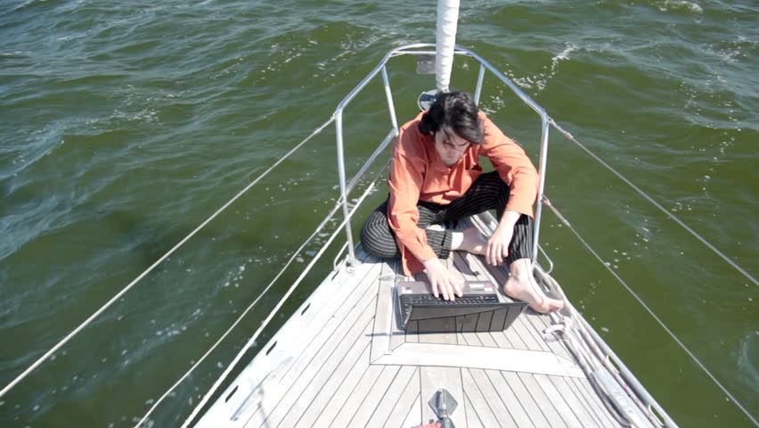 A young man working intently on a laptop on the nose yacht. Yacht racing over
