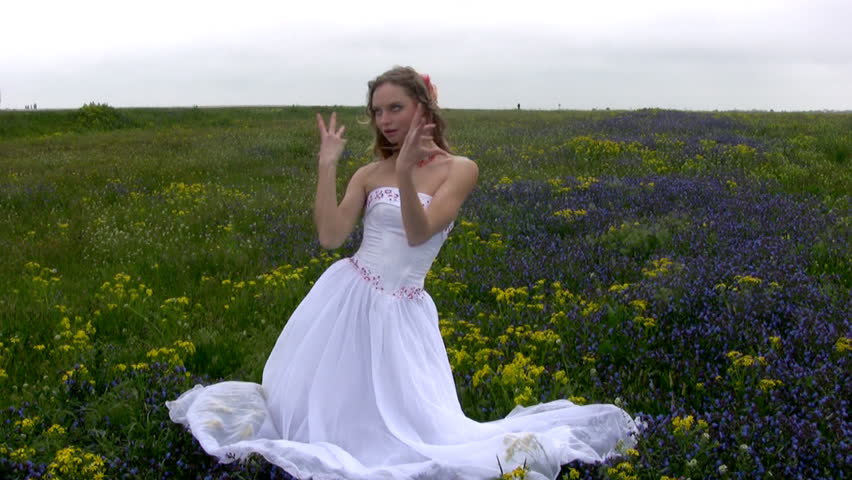 Graceful young bride in a white wedding dress dancing in a wild flower in the