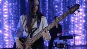Two young female musicians are playing bass guitar and drums on a stage with bright led lights in the background, creating a vibrant and energetic performance - Powered by Shutterstock - Get 15% off with code: PIKWIZARD15