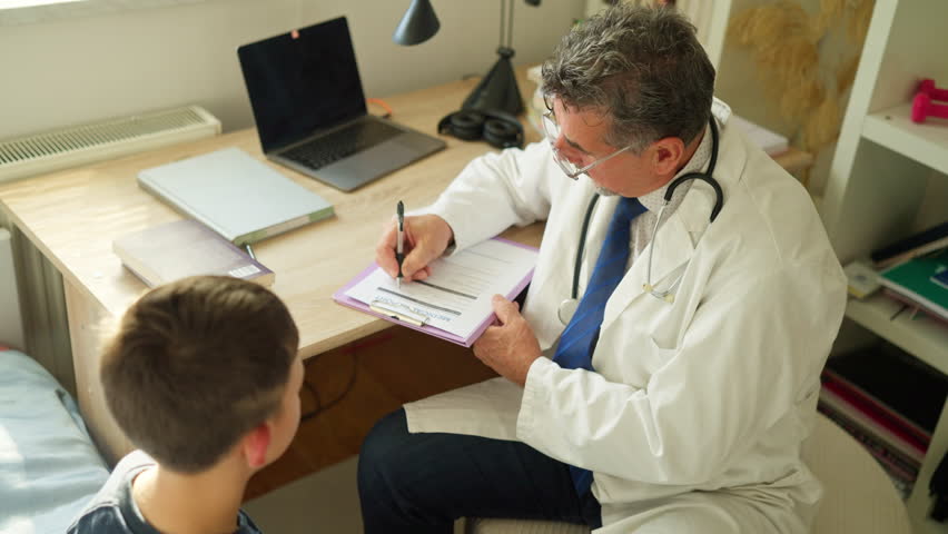 Pediatrician in a white coat sits at a desk, writing on a medical report while engaging with a young boy during a consultation. Concept of professional healthcare service, child-friendly medical care