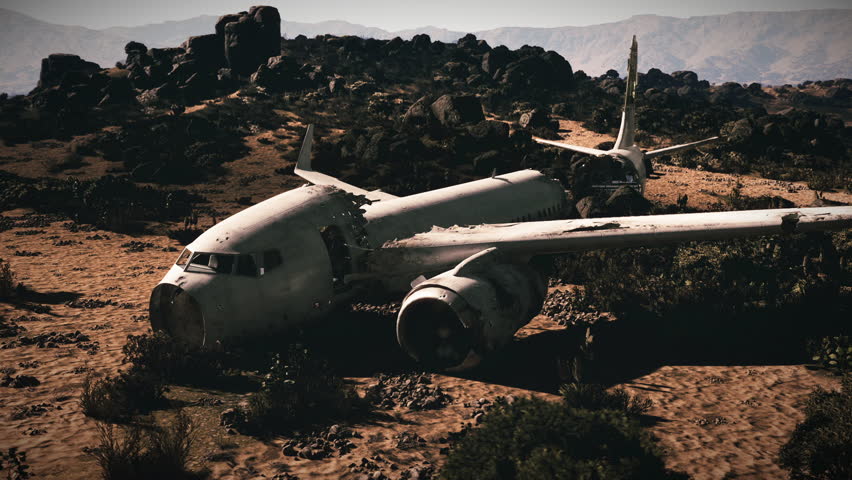 The damaged aircraft rests amid rugged terrain, surrounded by rocks and sparse vegetation, illustrating the aftermath of a severe aviation accident in a remote area.