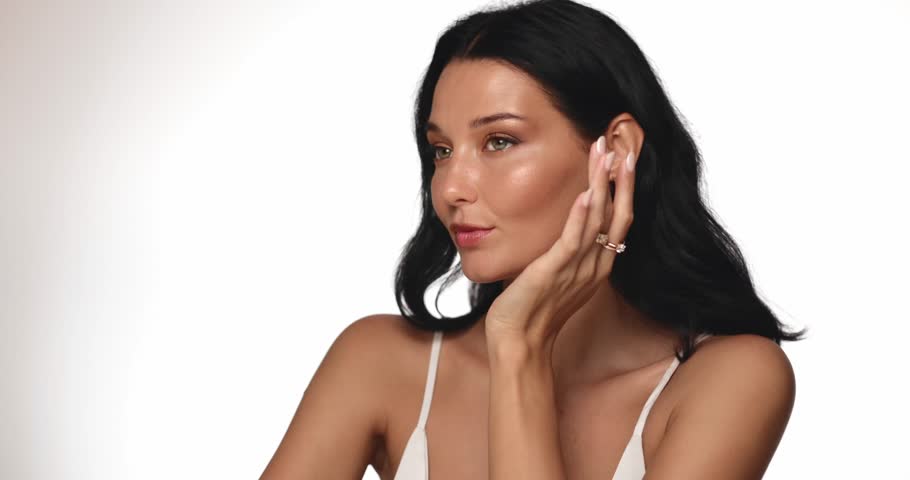 Sophisticated woman gently adjusting her makeup, showcasing glowing, flawless skin in a studio setting. Perfect for promoting beauty, skincare, or cosmetic product campaigns. 