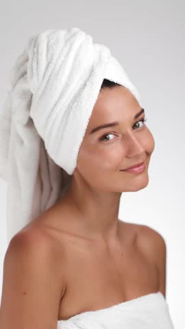 Elegant slow-motion clip of a woman in a towel turban softly touching her flawless skin, smiling with natural radiance. Perfect for beauty, skincare, or wellness product campaigns. 
