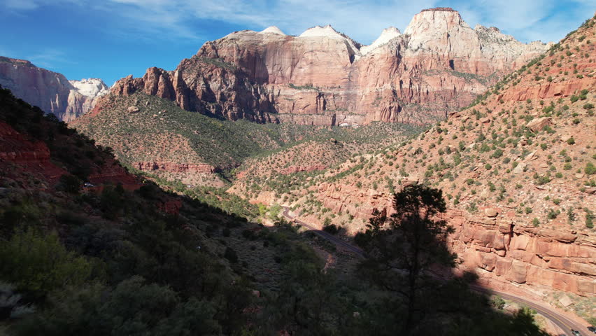 Flying through Zion Canyon, capturing red rock cliffs, lush greenery, and the winding roads beneath the towering sandstone formations.