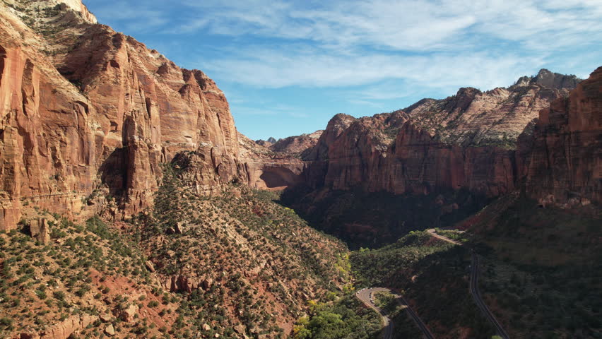 Aerial view of Zion Canyon with winding roads and towering red sandstone cliffs under a vibrant blue sky, capturing the scale and beauty of this iconic national park landscape.
