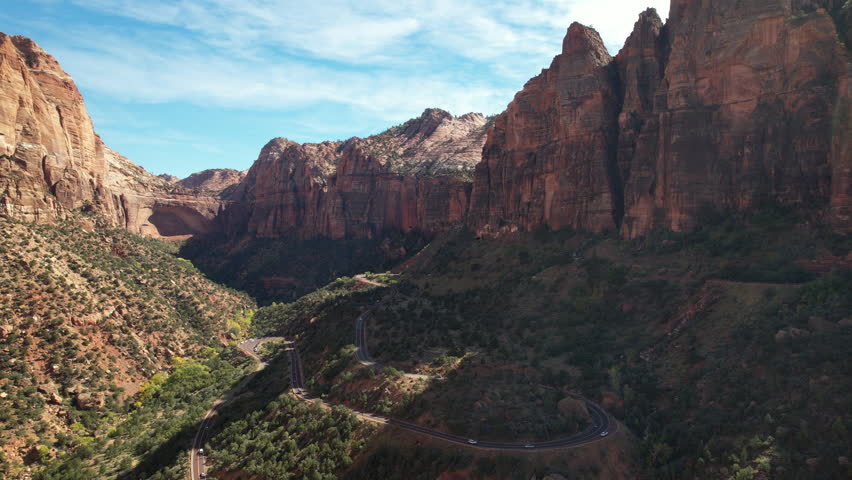 Aerial view of a winding road cutting through the majestic Zion Canyon, surrounded by towering red cliffs and vibrant greenery, showcasing the breathtaking landscape of Utah