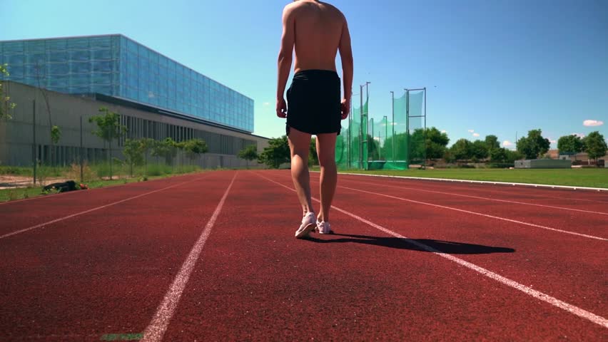 Rear view of a young male athlete running on an athletic track at a stadium. Man sprinting and training outside on a sports ground. Active endurance runner doing cardio