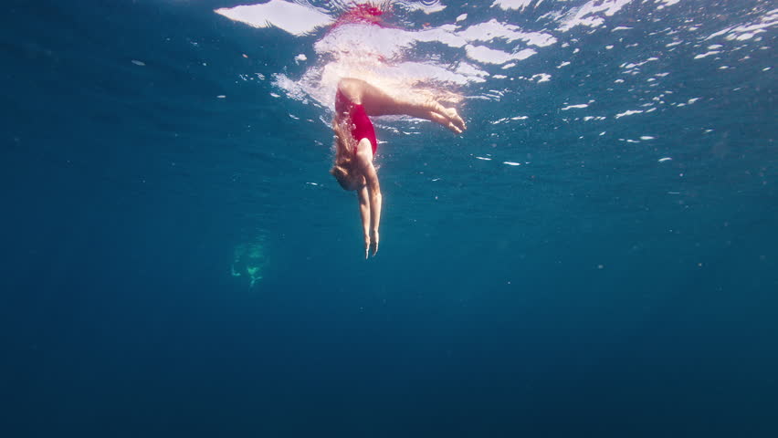 Teen girl in red suit dives and swims confidently underwater in the crystal clear tropical sea with sun shining through the water