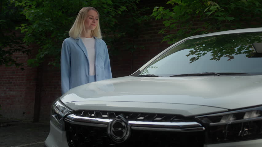 Cheerful satisfied Caucasian female automobile owner client woman girl buyer cuddle car lying on auto in city electric transport rent service businesswoman vehicle driver rejoicing new purchase smile