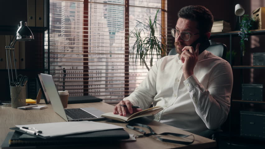 Caucasian man middle-aged guy worker speaking mobile phone call multitasking in office business conversation male corporate boss writing businessman trader planning executive work with laptop papers