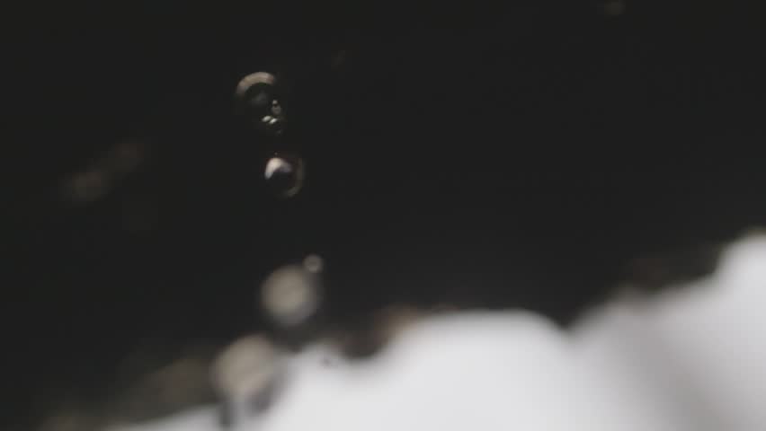 Crystal-clear water falls from rocks in slow motion, each droplet highlighted. The scene shows a spring waterfall, evoking themes of purity and relaxation.