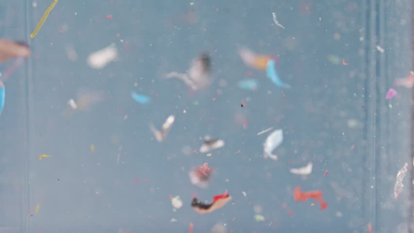 Microplastics suspended in water, close-up view in slow motion, highlighting the environmental and ecological impact of plastic waste.