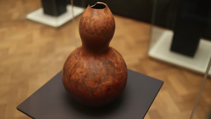 A beautifully crafted traditional gourd vessel with intricate carvings and patterns depicting scenes of cultural life. The natural tones enhance its historical and artistic value.