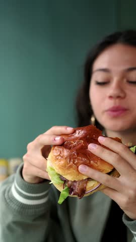 video portrait of young latina woman eating a hamburger and looking happy on camera