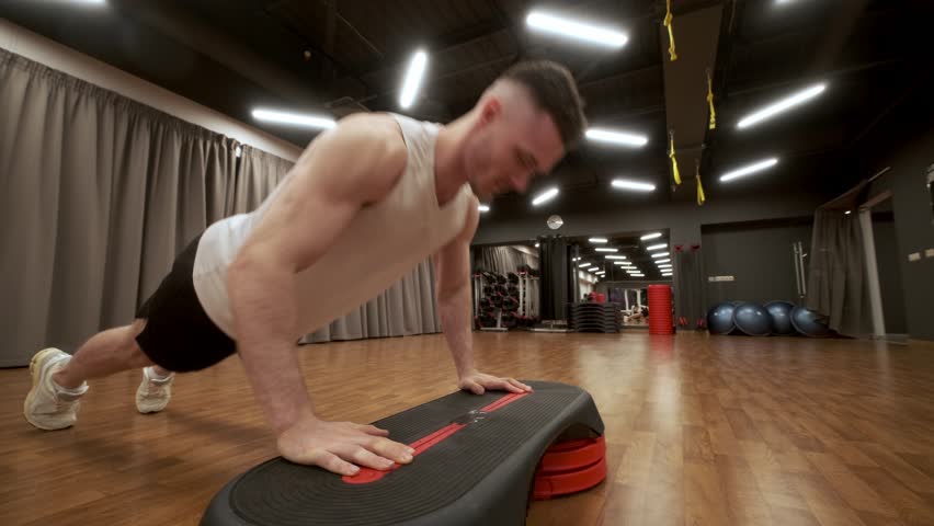 Muscular man in sportswear stretching body doing warm-up exercises on step platform exercising in gym or health club interior. Healthy active lifestyle concept