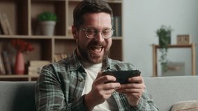 Bearded Caucasian gamer gadget addict man male guy play video game playing online mobile phone smartphone success yelling win internet winning gaming having fun at home couch sofa device entertainment - Powered by Shutterstock - Get 15% off with code: PIKWIZARD15