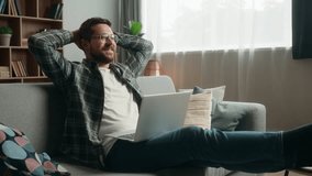 Happy smiling positive Caucasian man male guy at home couch sofa with laptop computer working online internet work typing shopping complete accomplishment done job relax break put hands behind head - Powered by Shutterstock - Get 15% off with code: PIKWIZARD15