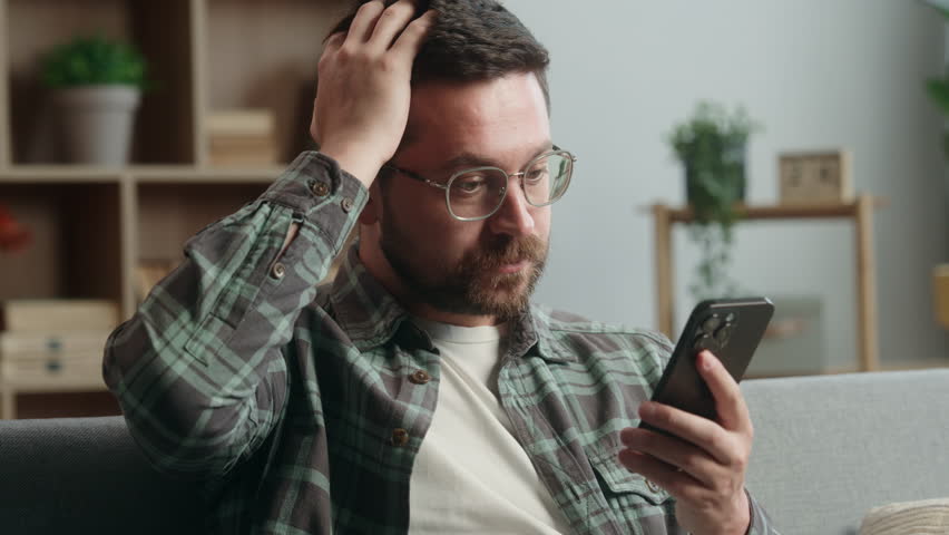 Caucasian man male guy user at home browsing mobile phone app social media smartphone shock bad news amazed trouble problem confused puzzled wonder online internet web at home couch sofa apartment