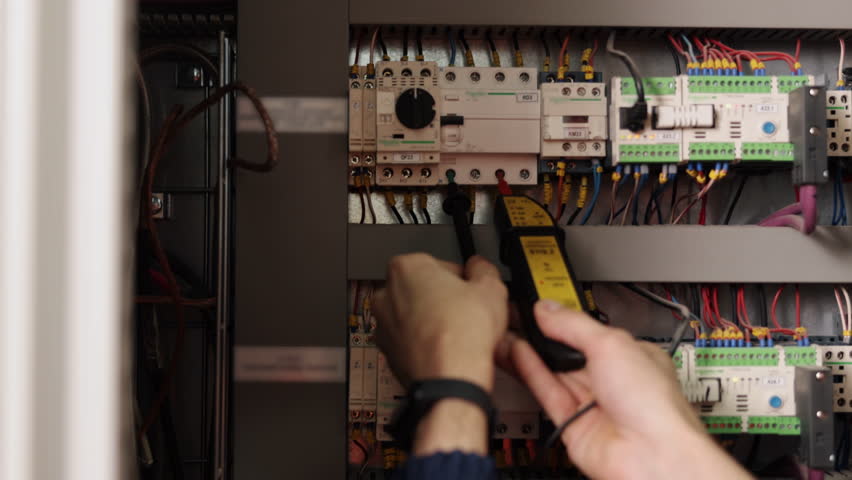Electrician testing, Electrical connections, Electrical repairs. Close-up electrician using multimeter to test electrical connections on circuit breaker panel with colorful wiring.