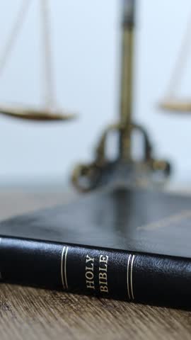 Holy bible book with ancient balance scales in the background. Vertical video. Close-up. Biblical concept of Christian Law, justice and judgment.