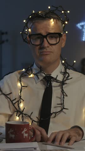 Sad corporate businessman working on Christmas day, he is wrapped in Christmas lights
