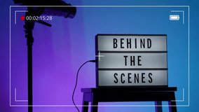Behind the scene light box in front of vdo camera frame. Black text on white lightbox of word Behind the scenes. Prop for filmmaker movie or film studio. Footage for B roll video production making of. - Powered by Shutterstock - Get 15% off with code: PIKWIZARD15