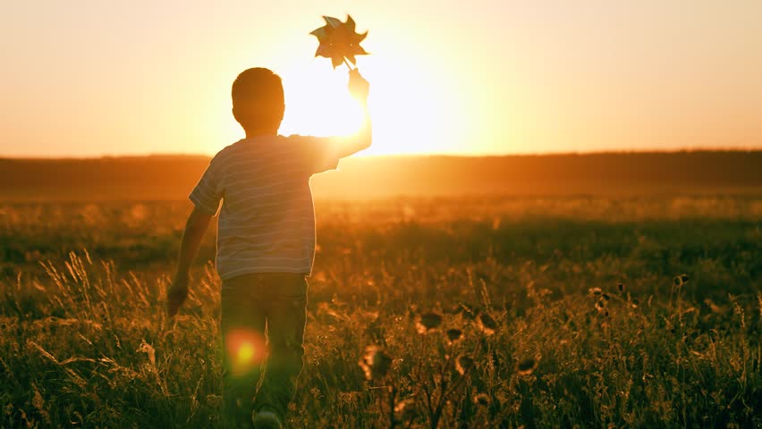 Happy child playing with toy pinwheel outdoor in summer in park Child boy runs with toy wind pinwheel in his hand on summer field, sun day, against sun sky. Childhood children. Family holiday, nature