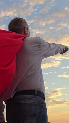 Superhero man WIth Red Cape Blowing in Wind Walks, Looking into Sunset, Ready to save world. Man playing in red cape against sunny sky. Super hero man meditating at sunset in against sky