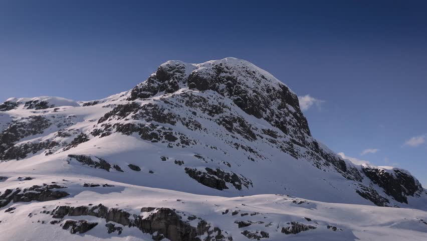 Aerial orbit shot of snowy mountain with summit against blue sky. Beautiful landscape in Norway, Europe.