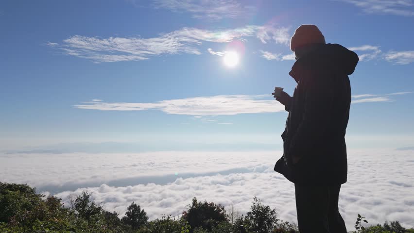 Hipster male hiker enjoying sunset on peak of foggy mountain. Tourist traveler