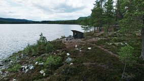 Family sitting around a campfire at a hiking hut (Slogbod), enjoying quality time together by a lake in Dalarna Sweden. Mother reads a book while father and son relax in nature. Aerial View - Powered by Shutterstock - Get 15% off with code: PIKWIZARD15