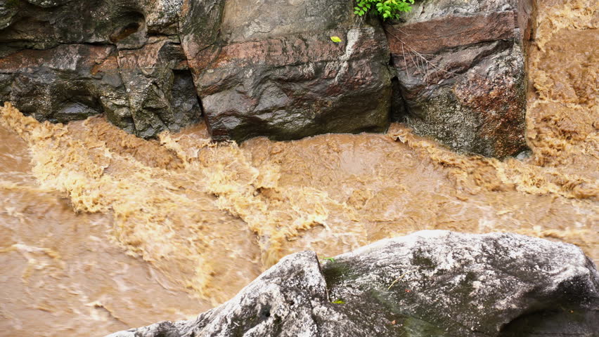 High-pressure flood water in mountain river tributary. A mountain river or stream raging in a flash flood. Upstream view over the turbulent waters.