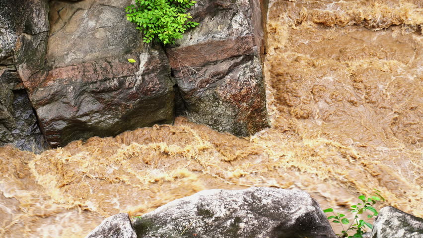 High-pressure flood water in mountain river tributary. A mountain river or stream raging in a flash flood. Upstream view over the turbulent waters.